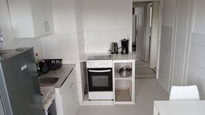 Een compacte keuken met witte kastjes, een inbouwoven, een koffiezetapparaat en een klein plankje met kookgerei.