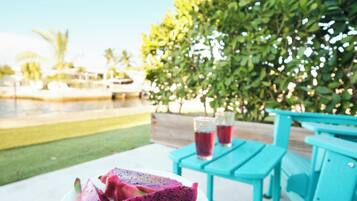 A table with a plate of dragon fruit and a glass of red beverage, outdoor seating, and a pool in the background.