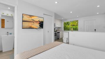 A modern bedroom with a bed, a TV on the wall, a bathroom, and a kitchen area.