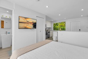 Une chambre moderne avec un lit, un téléviseur fixé au mur, une salle de bain et un coin cuisine.