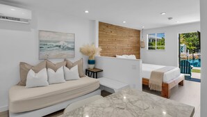 A modern bedroom with a bed, a sofa, a painting, and a view of a swimming pool.