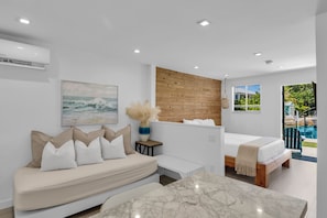A modern bedroom with a bed, a sofa, a painting, and a view of a swimming pool.