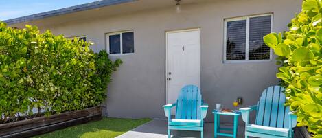 Una casa con puerta principal, dos ventanas, un jardín pequeño y un patio con dos sillas y una mesa.