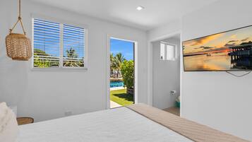 Un dormitorio con cama, ventana con persianas, puerta que da a una piscina y un televisor montado en la pared.