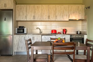 A kitchen with wooden cabinets, a stainless steel refrigerator, a microwave, a red kettle, and a dining table with chairs.