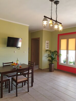 Un área de comedor con una mesa, sillas, un televisor, una planta y una ventana con marco rojo.