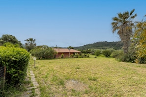 A house with a red roof, surrounded by greenery and a clear sky.