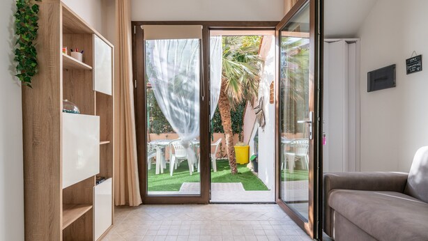 A room with a sliding glass door leading to a patio, a sofa, a wooden bookshelf, and a small table. - Holiday Home "Casa Clà" with Garden and Air Conditioning (Villasimius)
