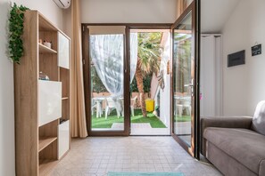Een kamer met een schuifdeur naar een terras, een bank, een houten boekenkast en een kleine tafel.