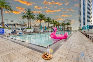 Une piscine avec un flotteur en forme de flamant rose, des palmiers et, au loin, un immeuble de grande hauteur.