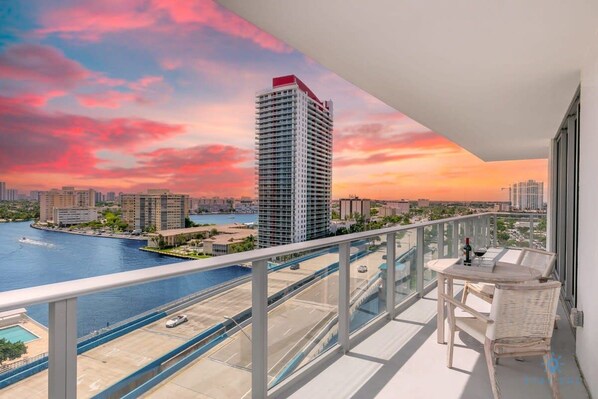 A balcony with a view of a city skyline, a body of water, and a sunset.
