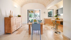 Une cuisine moderne avec une table à manger en bois, deux tabourets de bar et une vue sur l’extérieur.