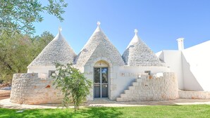 Un bâtiment en pierre doté de trois toits coniques, d’une porte centrale et d’un petit arbre au premier plan.