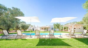 A pool area with lounge chairs and umbrellas, a white building with a conical roof, and a well-maintained lawn.