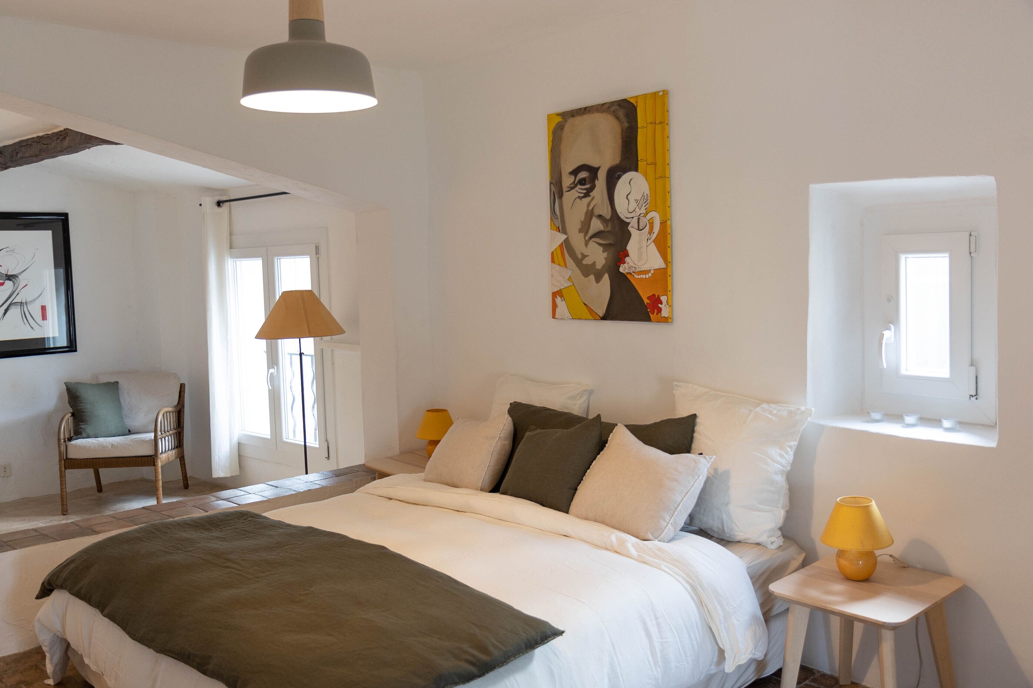 Een slaapkamer met een bed, een stoel, een lamp en een schilderij aan de muur.