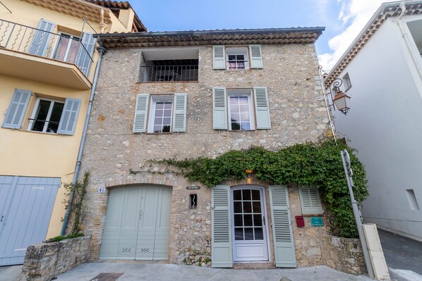 A two-story building with a stone facade, green shutters, and a small balcony.