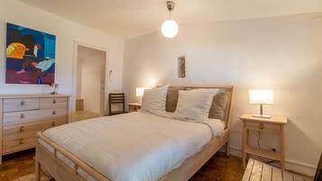 A bedroom with a large bed, two bedside tables with lamps, a wooden dresser, and a painting on the wall.