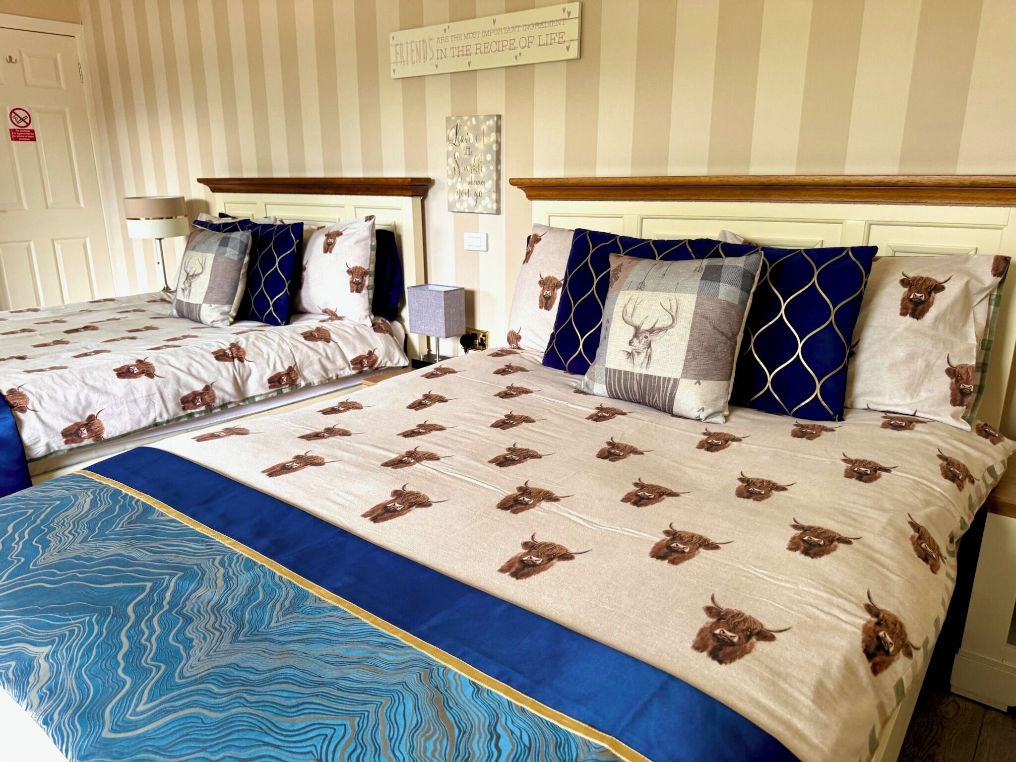 Une chambre d’hôtel avec deux lits, un papier peint à rayures, un panneau accroché au mur et un couvre-lit bleu à motifs.