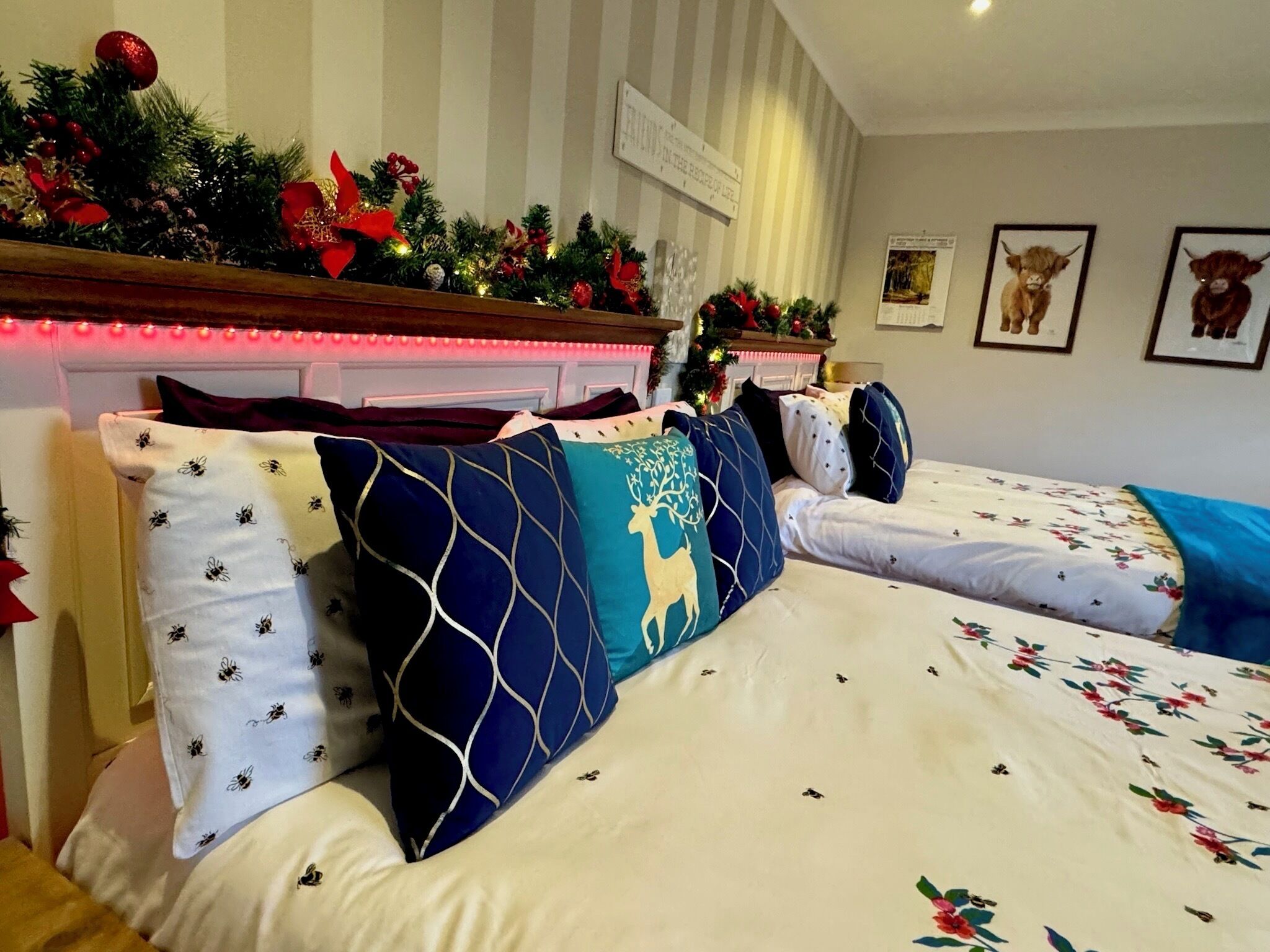 Une chambre d’hôtel avec deux lits, chacun agrémenté de draps à motifs floraux et de coussins décoratifs. Un sapin de Noël et des décorations festives ornent la tête de lit.