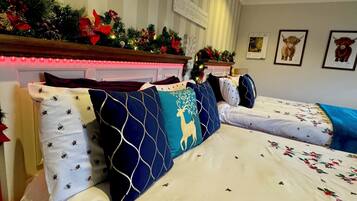 Une chambre d’hôtel avec deux lits, chacun agrémenté de draps à motifs floraux et de coussins décoratifs. Un sapin de Noël et des décorations festives ornent la tête de lit.