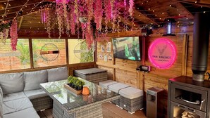 A cozy retreat room with a sofa, a glass-top table, hanging floral decorations, a fireplace, and a TV screen. - FINN VILLAGE Mountain View Cottage Garden & XXL HOT TUB (Glasgow)