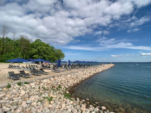 Une plage avec des chaises longues et des parasols, un rivage rocheux et une vue dégagée sur la mer.