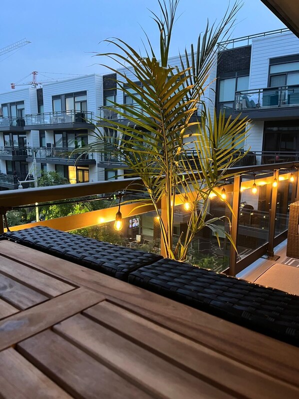 A balcony with a wooden floor, a potted plant, and string lights.