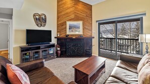 A living room with a fireplace, a television, and a balcony with a view of trees. - Location, Amenities and Value!  Near Ski Area Split Level Condo, Access to Pool, (Steamboat Springs)
