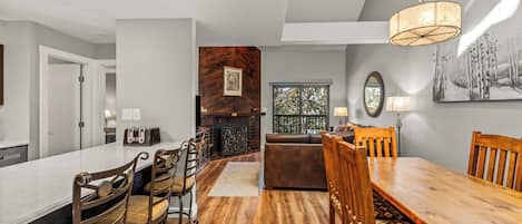 A modern kitchen with a dining area, wooden flooring, and a large window.
