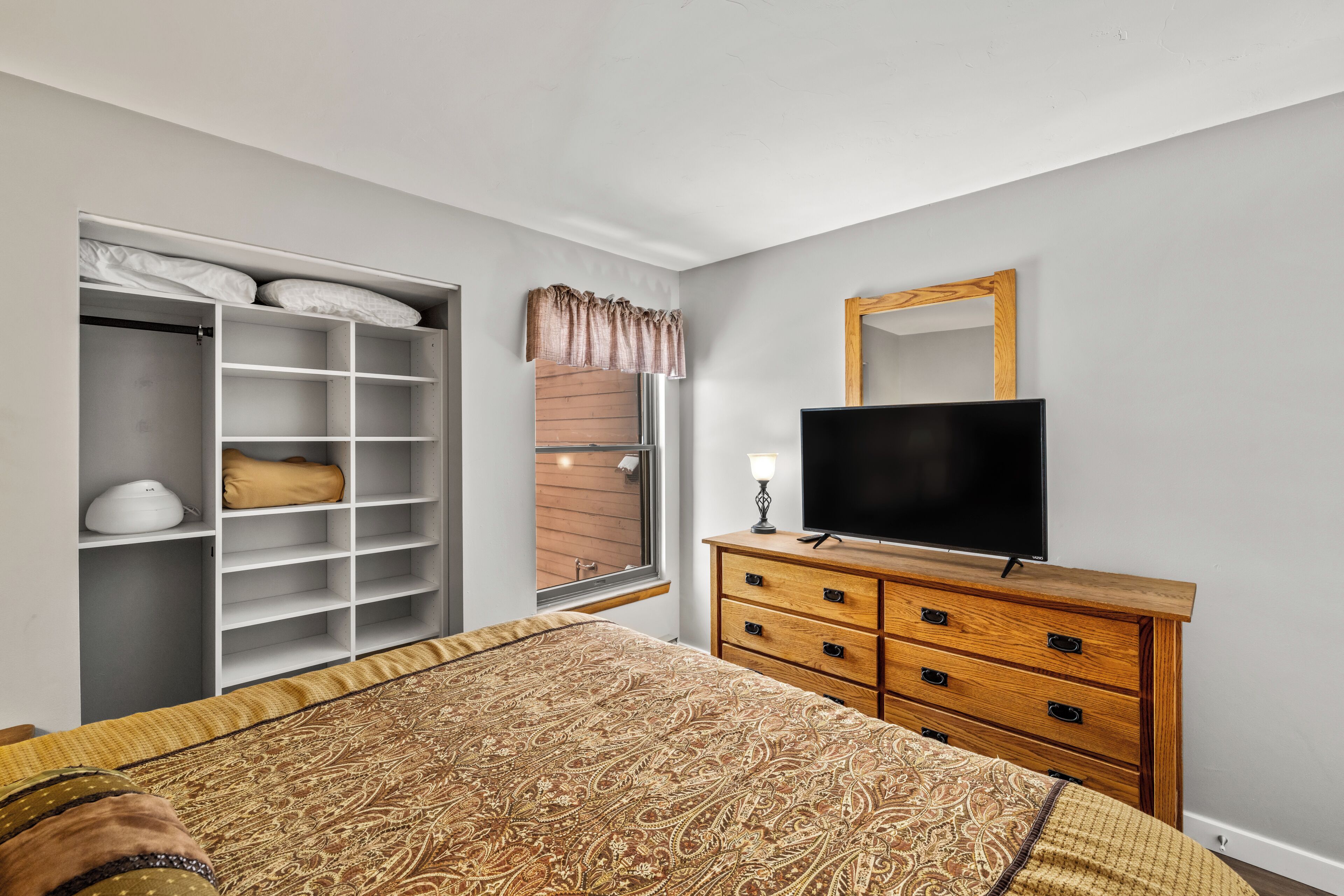 A bedroom with a bed, a TV, a wardrobe, and a window.