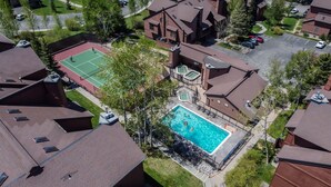 An aerial view of a residential area with a swimming pool surrounded by houses, a tennis court, and a parking lot. - Location, Amenities and Value!  Near Ski Area Split Level Condo, Access to Pool, (Steamboat Springs)