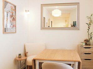 Een eethoek met een houten tafel, een witte stoel, een bijzettafeltje met een plant en een spiegel aan de muur.