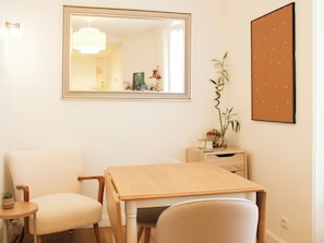 A room with a wooden table, two chairs, a mirror, a corkboard, and a small plant.