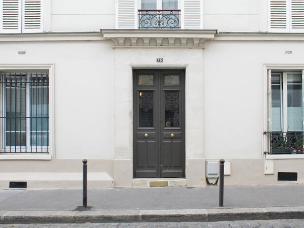 A building facade with a central dark-colored door, white shutters, and a balcony with metal railings.