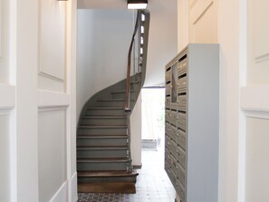 A staircase with a wooden handrail leading to a landing, flanked by a wall with a light switch and a row of metal lockers.