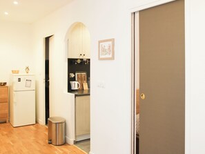 A compact kitchen with a refrigerator, a kettle, and a trash bin.