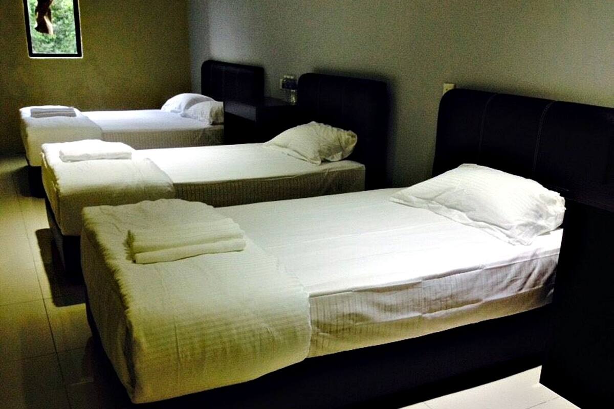 A hotel room with three single beds, each with a white bedspread and pillows.