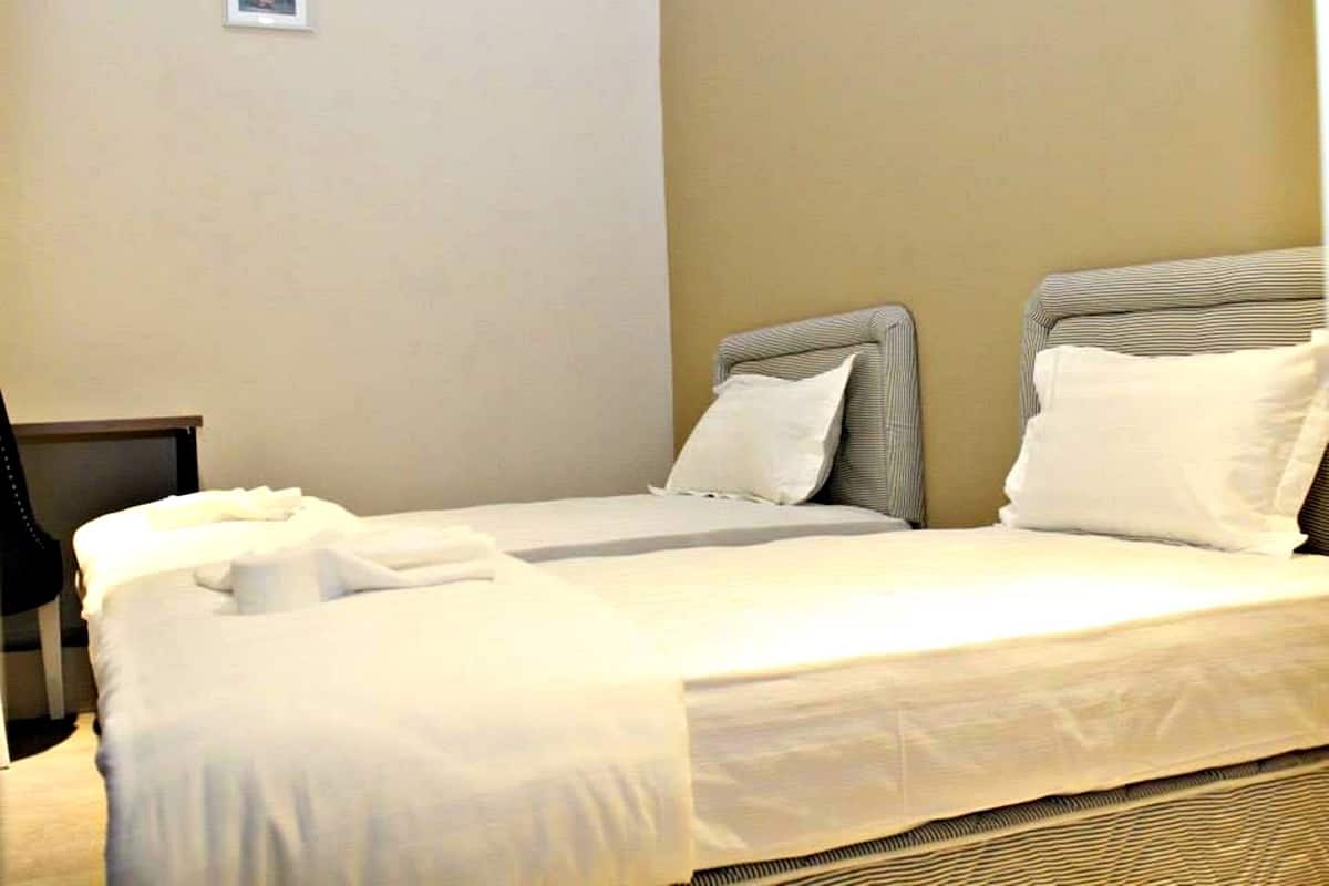 A hotel room with two single beds, a nightstand, and a chair.