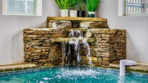 Una cascada de piedra en un área de piscina, con un muro de piedra y plantas en macetas en la parte superior.
