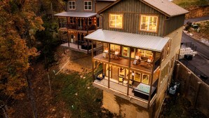 Una cabaña de troncos de dos pisos con un balcón y una terraza, rodeada de árboles.