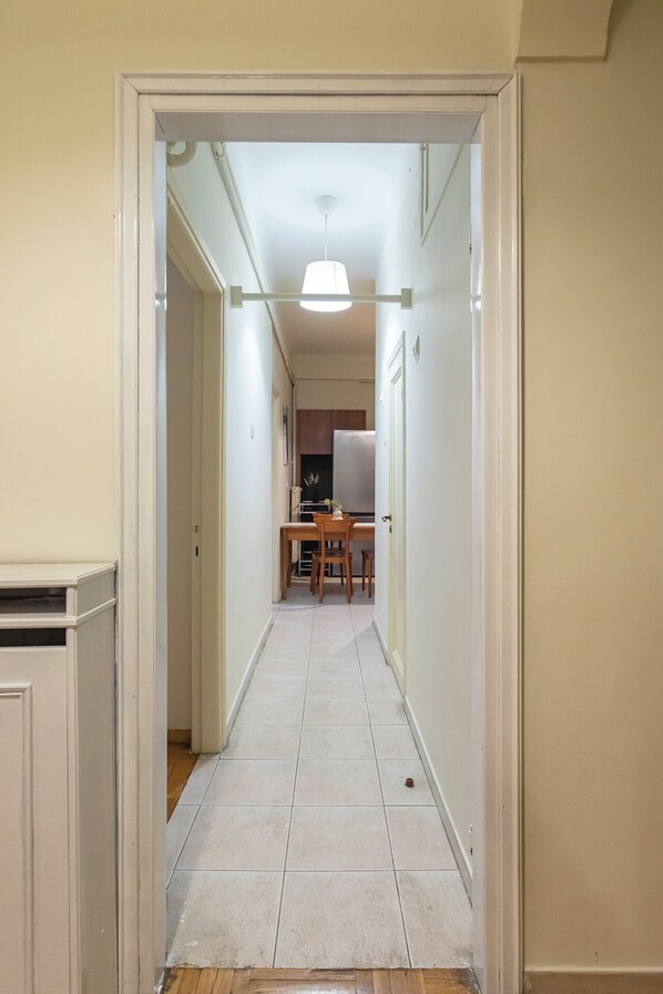 A narrow hallway with a dining area at the end, featuring a table and chairs.