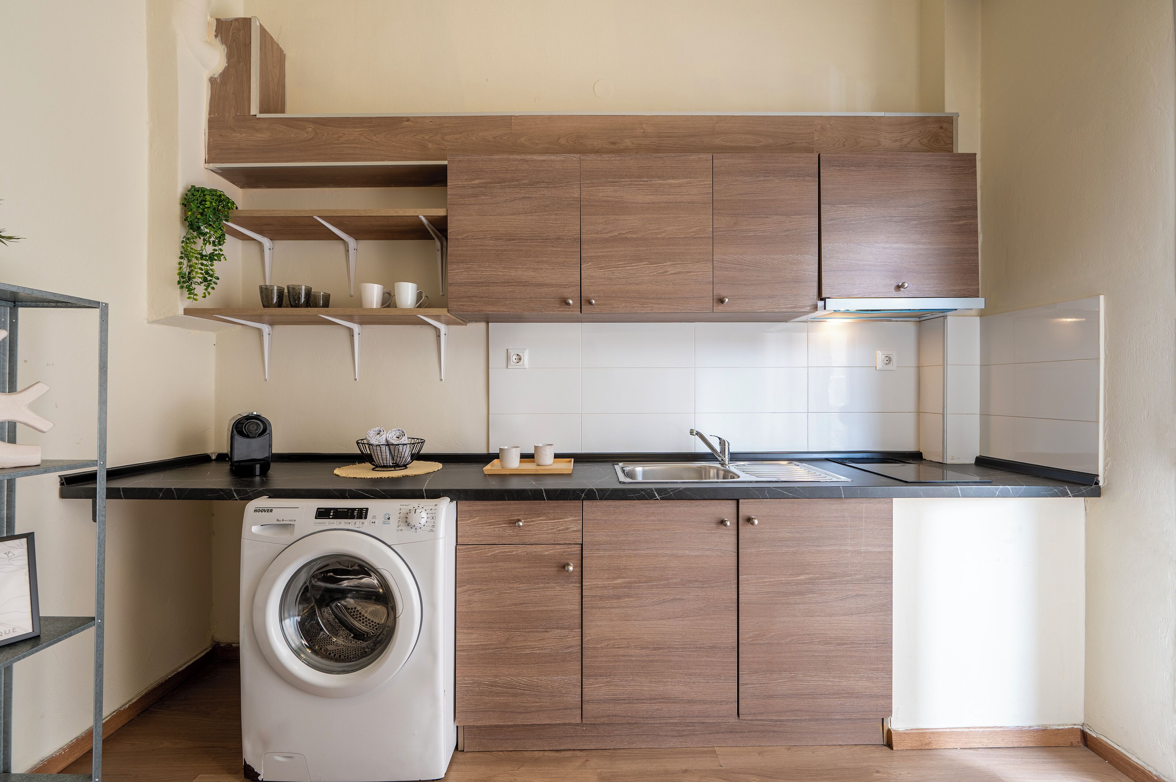 Een kleine keuken met een wasmachine, houten kastjes, een spoelbak en een aanrecht.