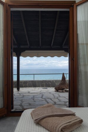 Une chambre avec un lit, une vue sur l’océan et une terrasse en pierre à l’extérieur.