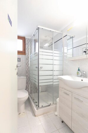 Une salle de bain moderne avec une douche à parois de verre, des toilettes blanches et un meuble-lavabo doté d’un miroir et d’un évier.