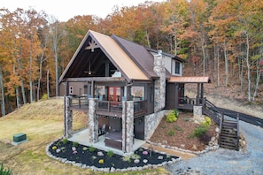 A two-story cabin with a stone foundation, a balcony, and a covered deck.