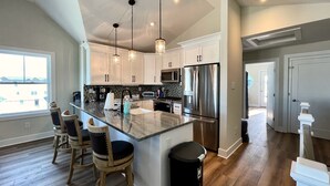 A modern kitchen with a large island, stainless steel appliances, pendant lighting, and a view of the outside. - Stunning  Townhome, Private Elevator, Expansive Bay Views! (Sea Isle City)