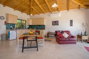 A spacious living area with a wooden ceiling, a dining table with chairs, a red leather sofa, and a kitchen with wooden cabinets and a window. - David's Villas - Villa Angela Open Plan with infinity Pool (Zakynthos)