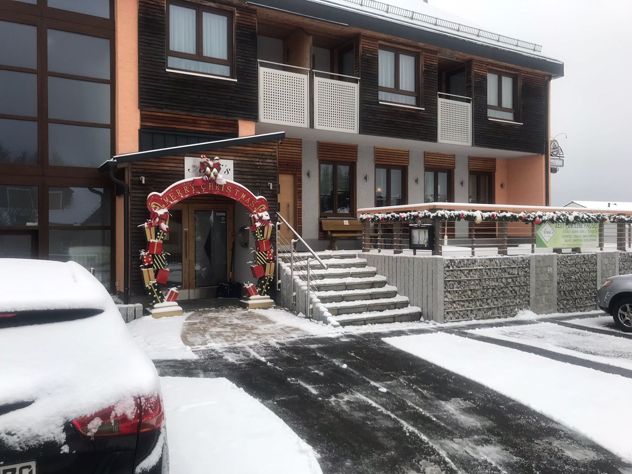 Ein Gebäude mit einem weihnachtlichen Bogen am Eingang und einer Treppe, die zum Eingang führt, sowie ein mit Schnee bedeckter Boden.