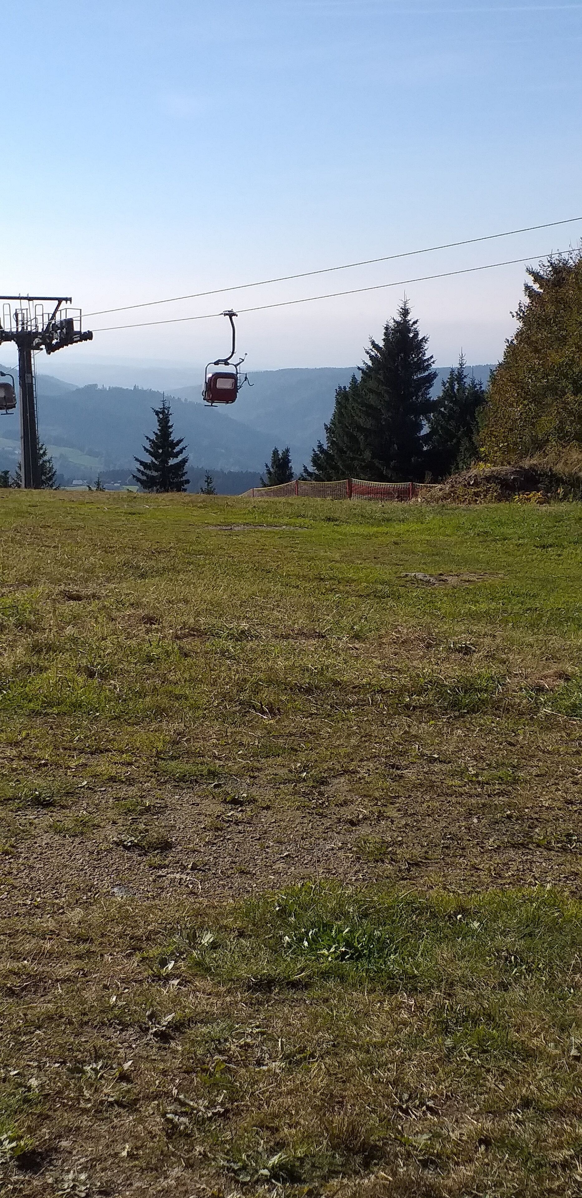 A ski lift chair suspended above a grassy area with a mountainous backdrop.