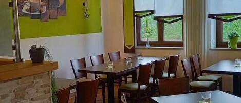 Un restaurant avec des tables et des chaises en bois, un comptoir en pierre et des murs verts ornés d’un tableau.